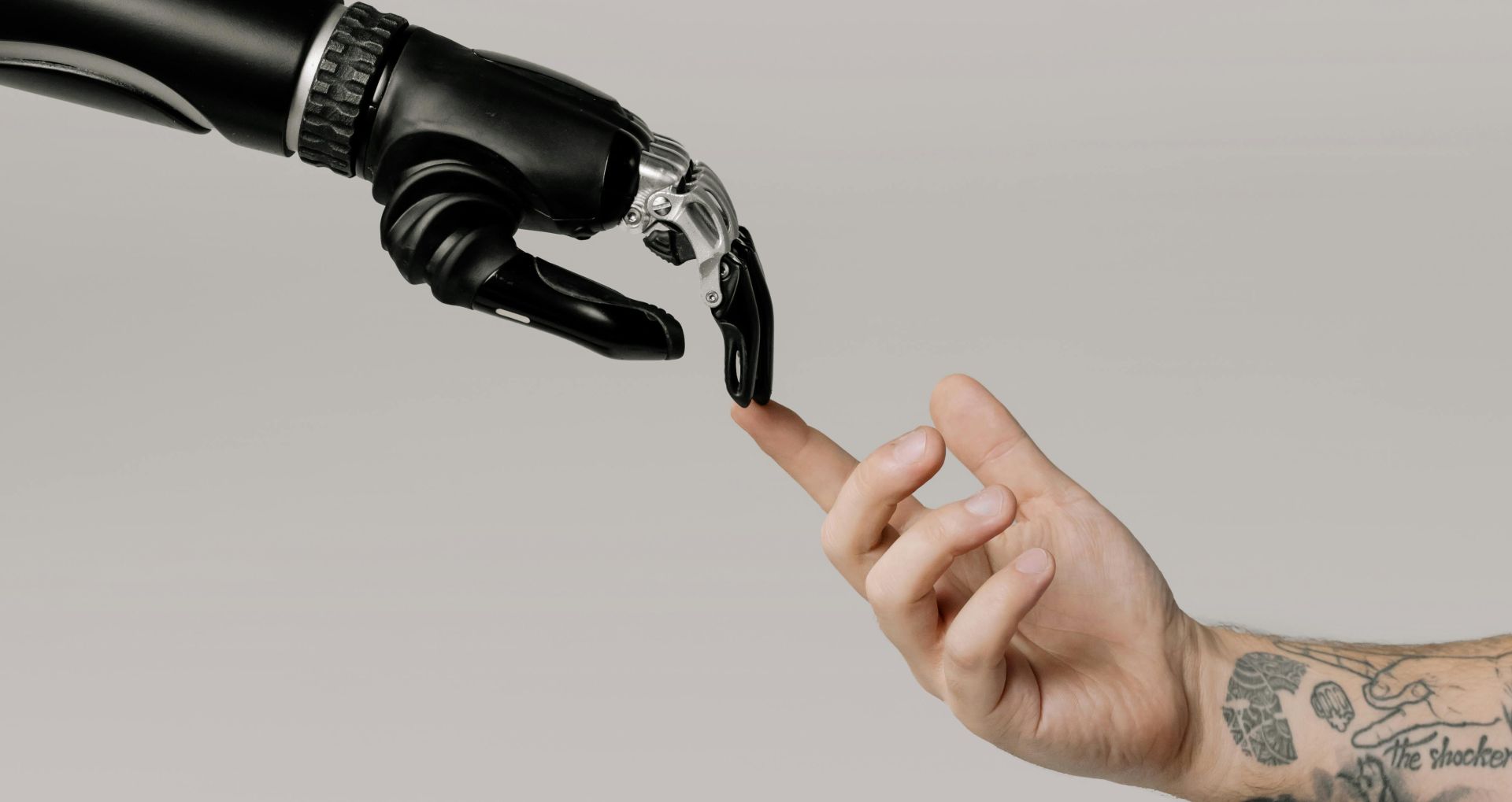 A human hand with tattoos reaching out to a robotic hand on a white background.
