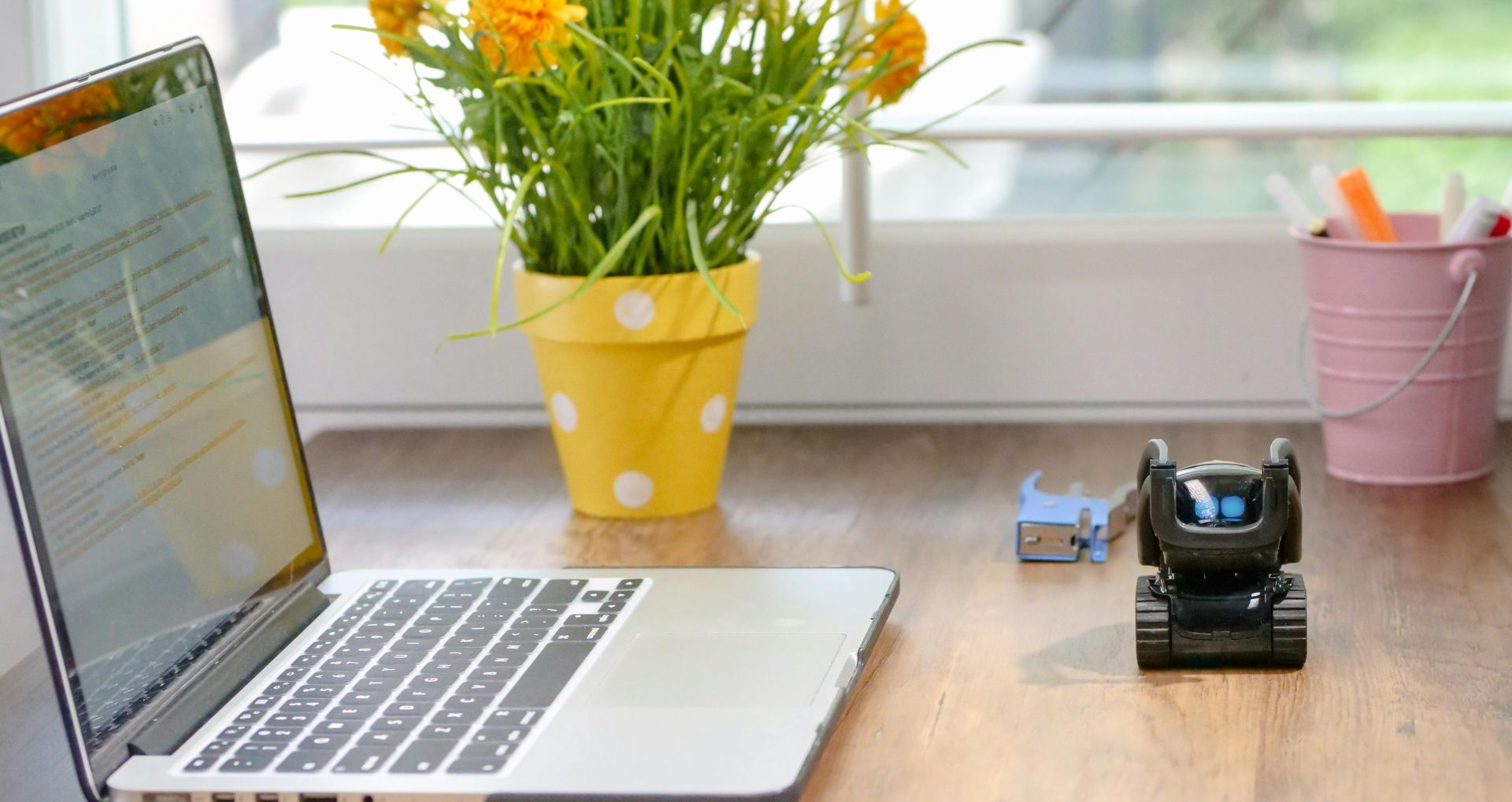 Stylish workspace featuring a laptop, toy robot, and vibrant flowers in natural light.